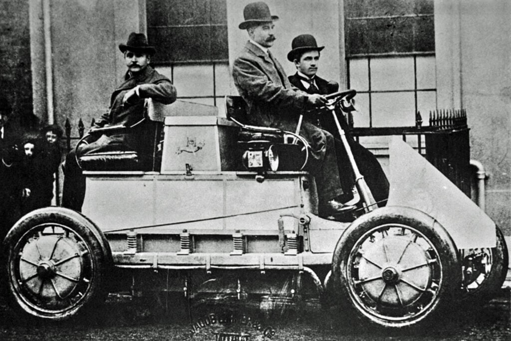 black and white photo of 3 men sitting on the first car