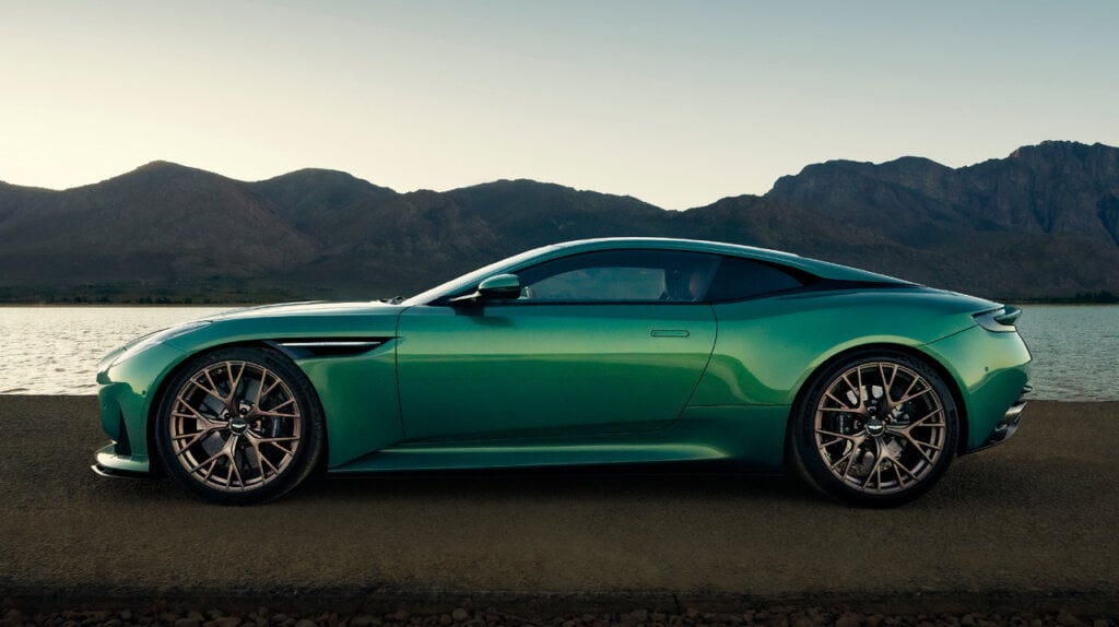 Green Aston Martin DB12 Super Tourer side profile on a beach next to the ocean