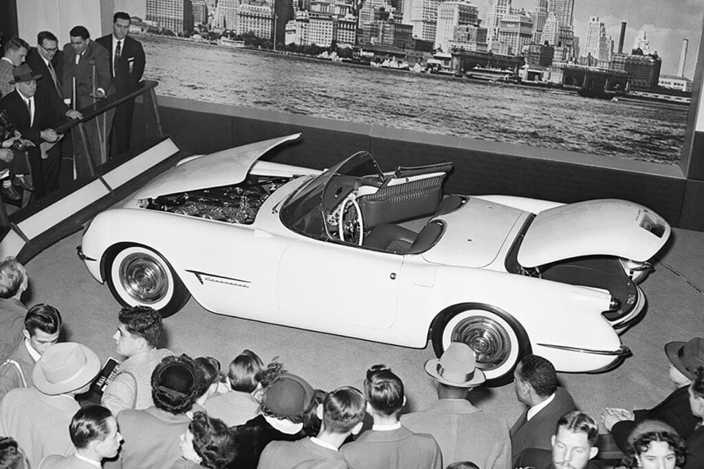 a car being shown in front of a group of people black and white