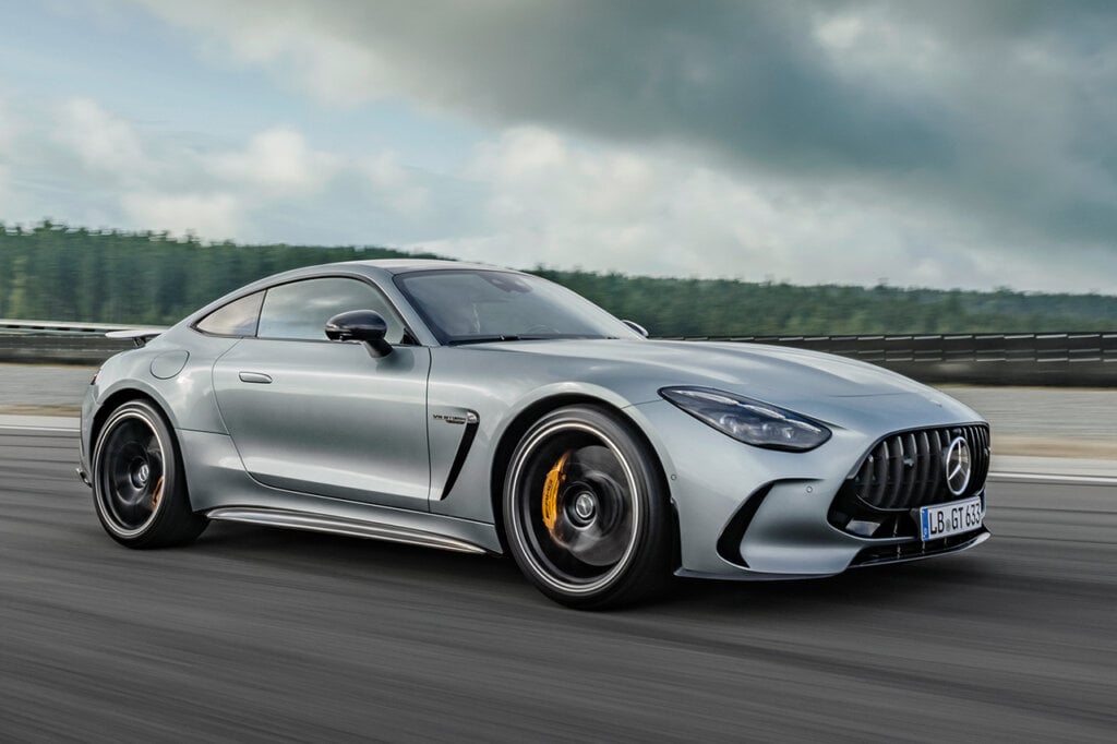 silver mercedes AMG GT Coupe driving on asphalt runway and cloudy sky behind it