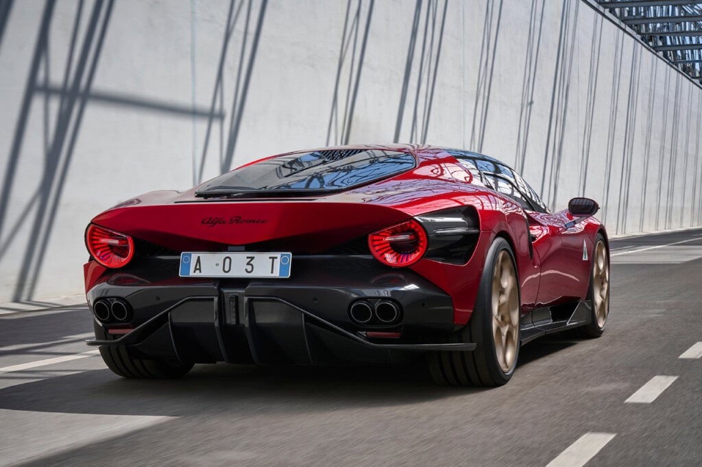 Red Alfa Romeo 33 Stradale cruising down a street with a white wall with shadows to the left of it