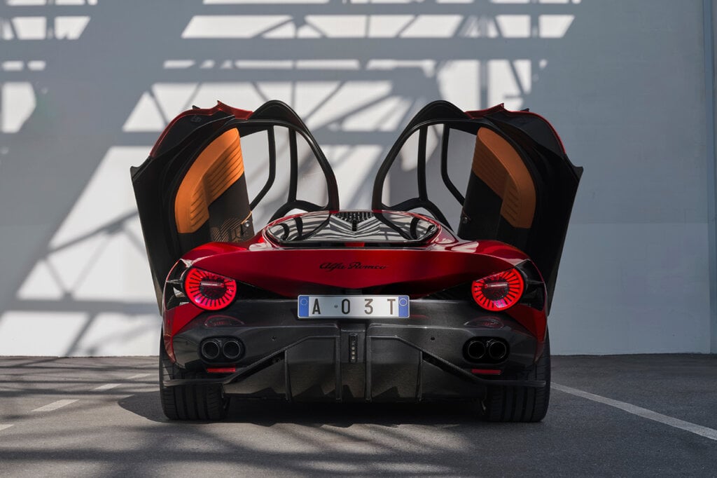 Rear end of a red Alfa Romeo with doors opened infront of a white wall