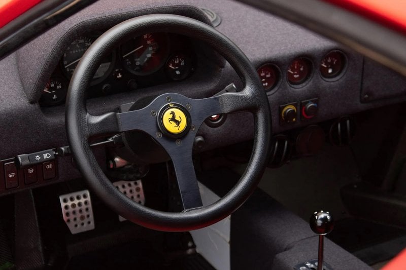 Steering wheel with the yellow Ferrari Badge on the center of it, all black interior and manual stick shift in the center console