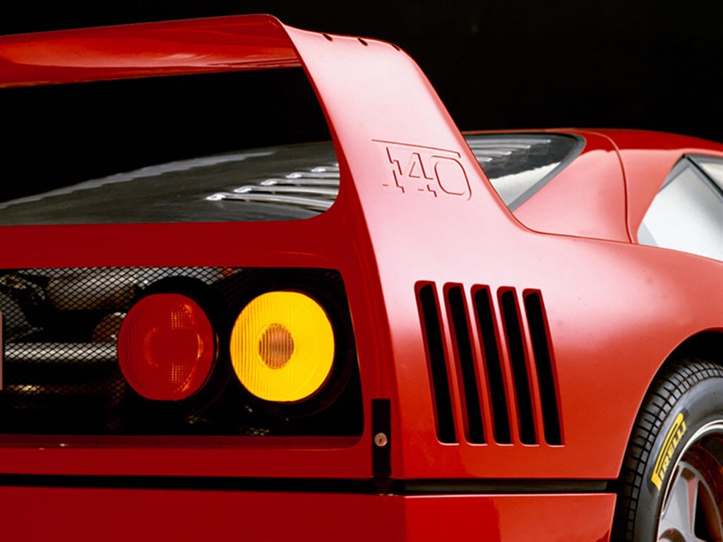 Rear detail shot of a red car with stamped F40 on the spoiler wing, black background and red and yellow taillights