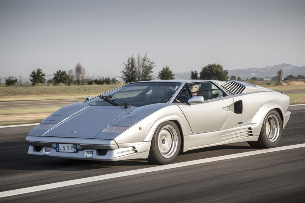 Silver Countach driving fast on the highway, overcast sky behind it