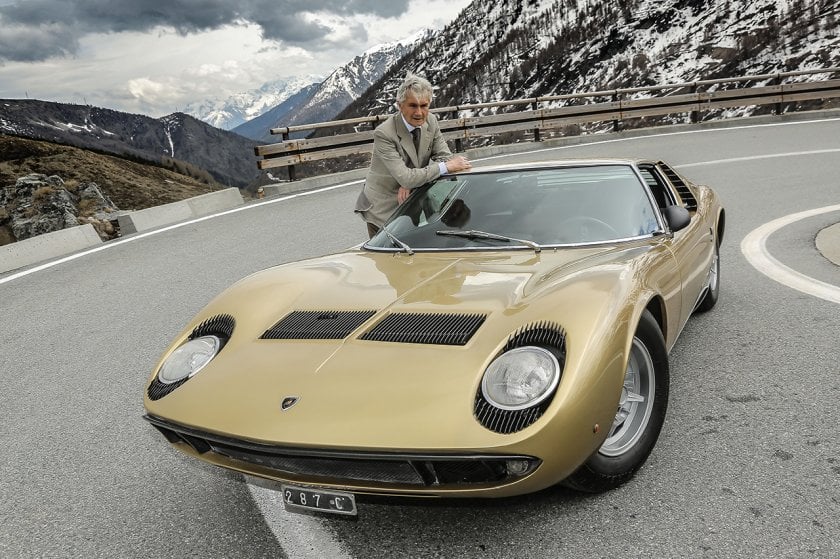 Designer Marcello Gandini next to a gold Lamborghini Miura with snowy mountains behind him