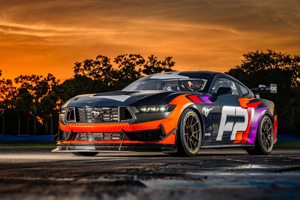 Orange and black Mustang GT4 on racetrack with sunset behind it