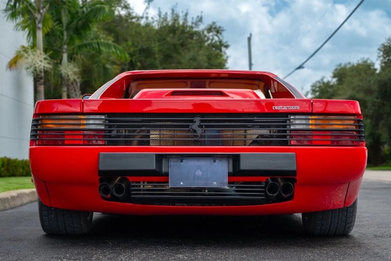 Rear end of a red Ferrari Testarossa palm trees and cloudy blue sky in the back