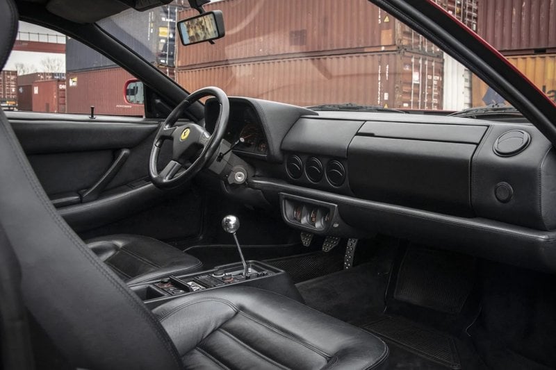 Black interior of a Ferrari 512M Testarossa surrounded by many shipping containers