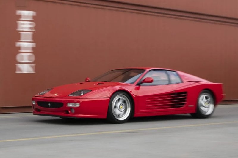 Red Ferrari Testarossa driving fast past some brown shipping containers with white letters