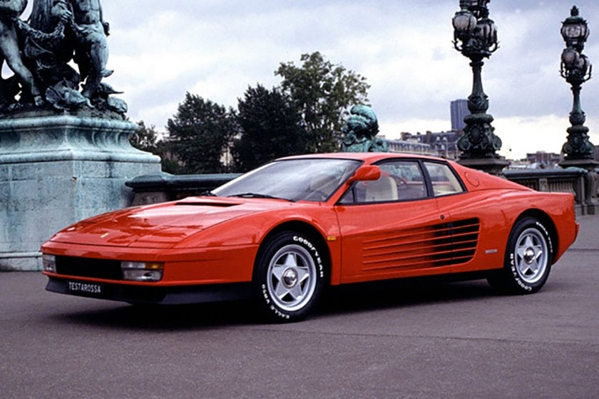 Red Ferarri Testarosso parked by a statue and some light poles