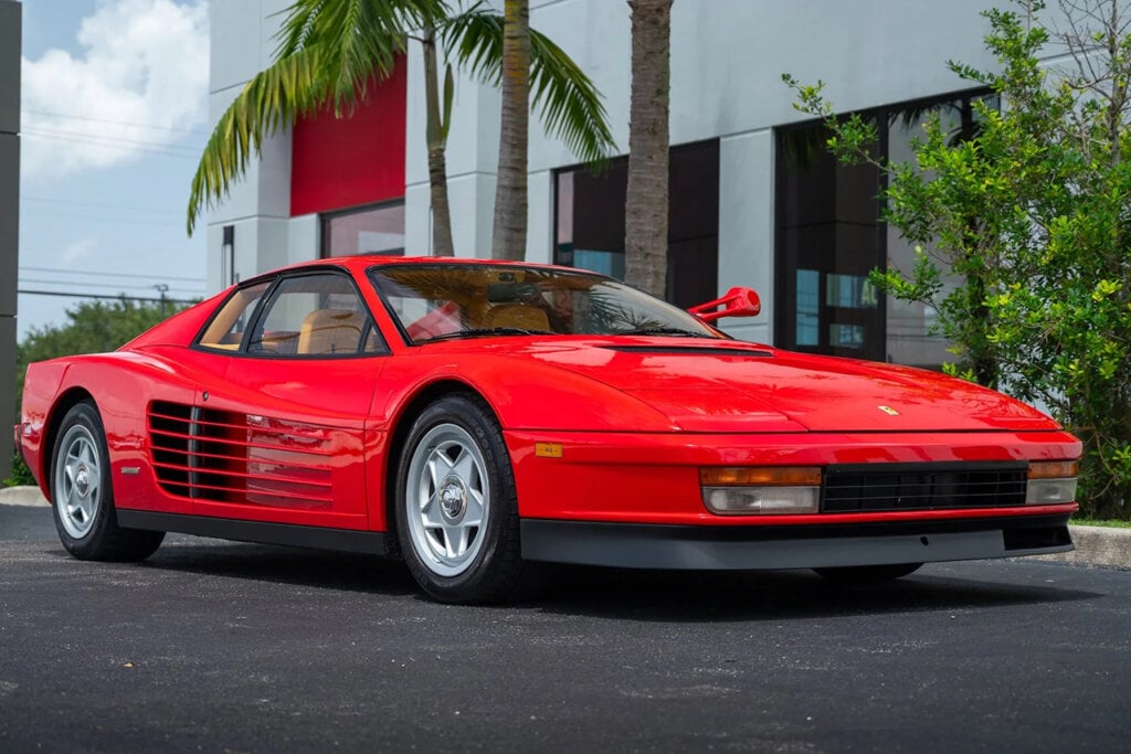 Red Ferarri Testarossa sitting in front of a white building and palm trees
