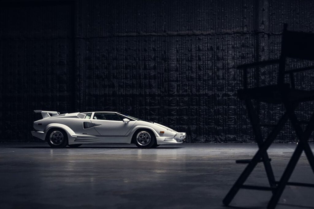 white Lamborghini countach with directors chair in front of it dark black background