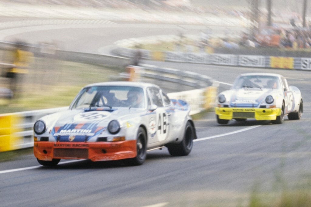 Two Race cars driving fast with people in background