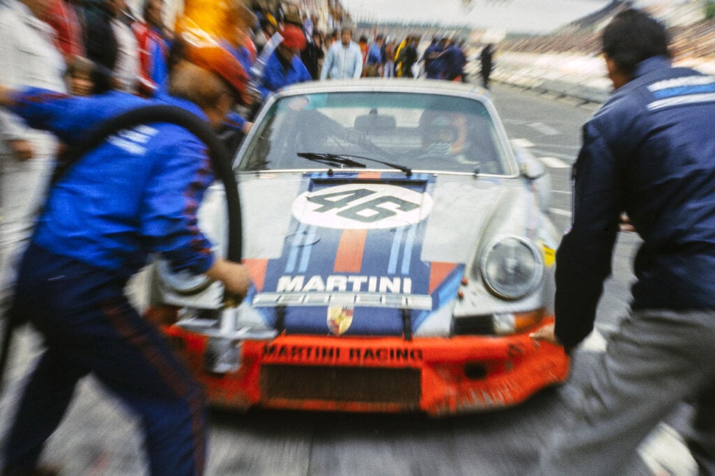 Porsche Race car with number 46 pulling into the pits 2 men infront of the car