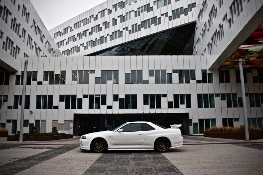white Nissan skyline r34 car in front of building with windows