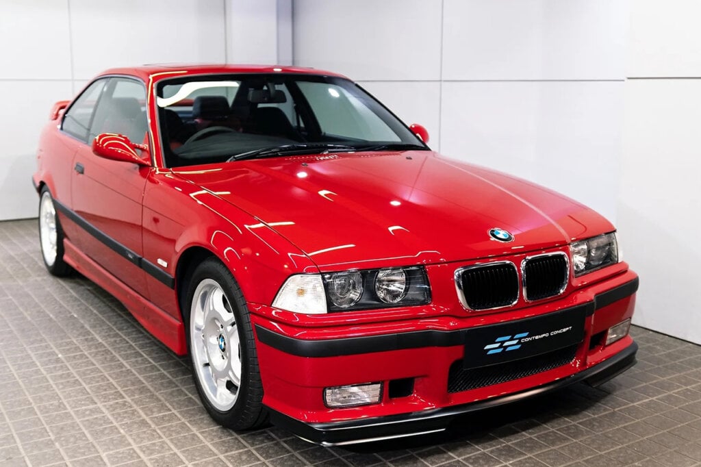 Red Imola BMW E36 M3 parked on brown tile and two white walls behind it