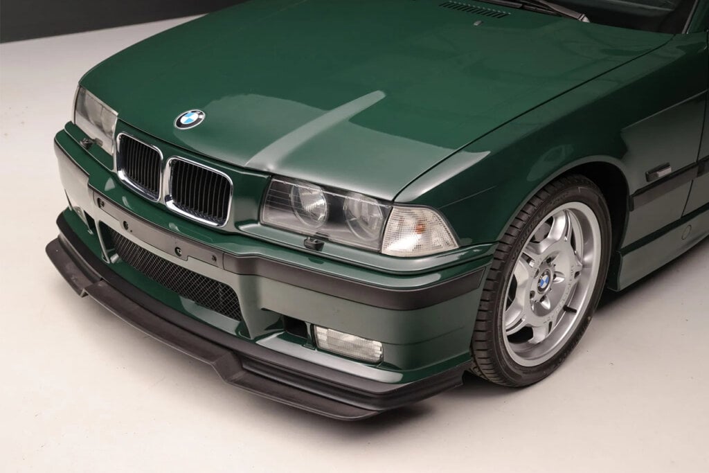 closeup of green BMW E36 m3 with a black front lip parked on white floor