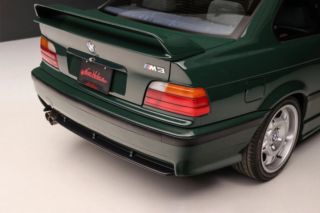 Rear end of a green BMW M3 it has a black license plate paper with red writing on it
