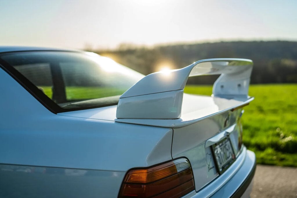 white spoiler wing on a BMW e36 m3 sun hitting the edge of it with grass in background