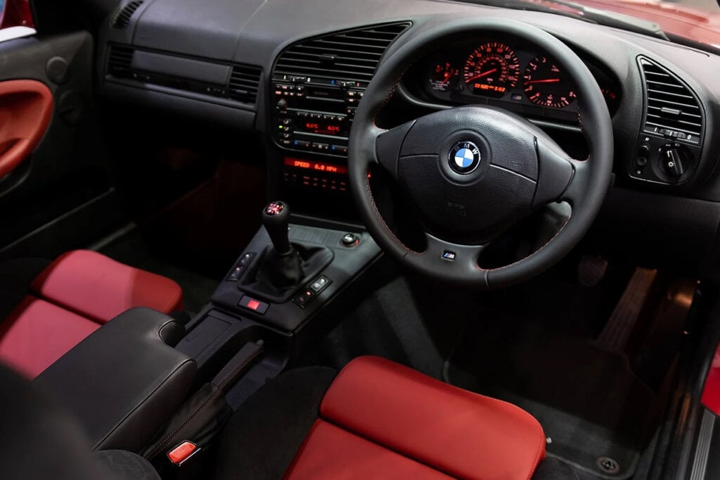 black steering wheel and black dashboard with red and black suede seats of a BMW e36 M3