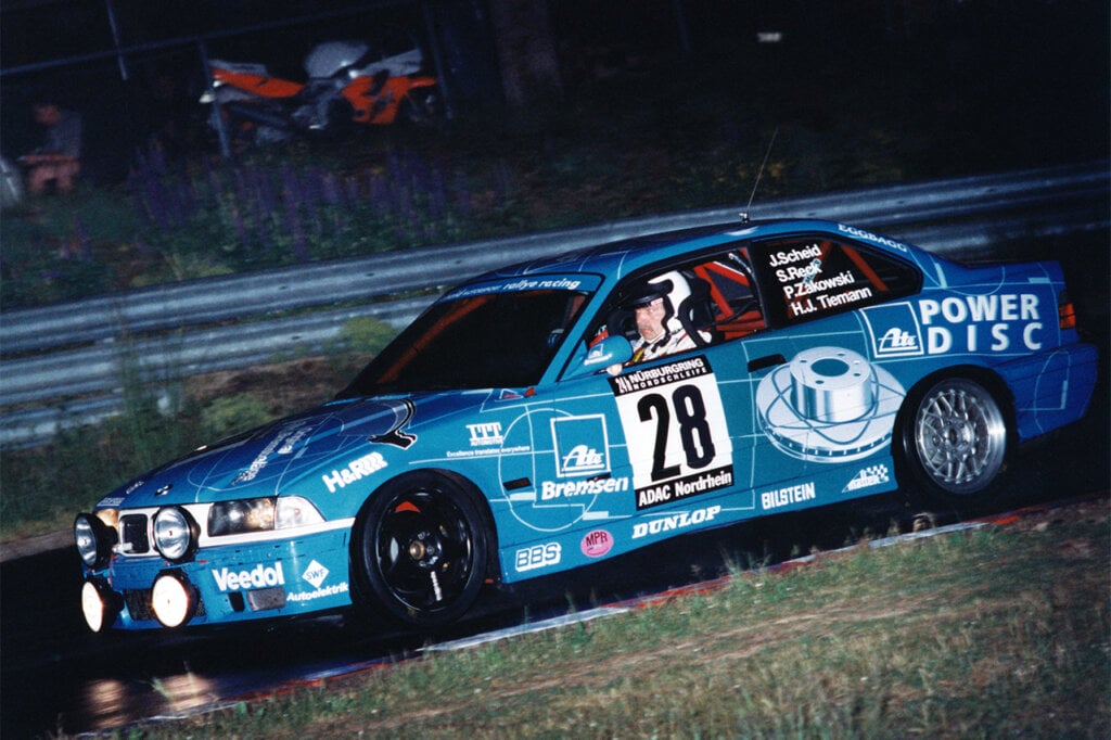 blue BMW e36 M3 race car taking a turn and a man focused on the turn at night