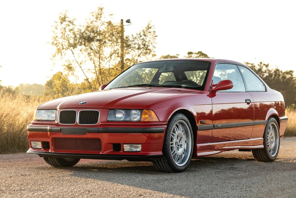 Red BMW E36 M3 parked infront of trees and a sunset