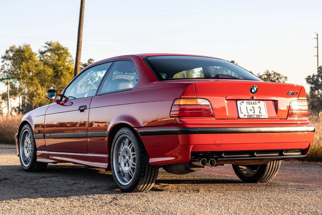 Rear end of a red BMW E36 M3 with the sun shining on the right side of the car