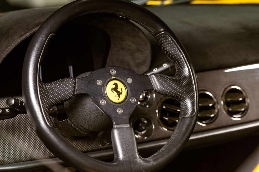 Ferrari F50 steering wheel next to carbon fiber dash