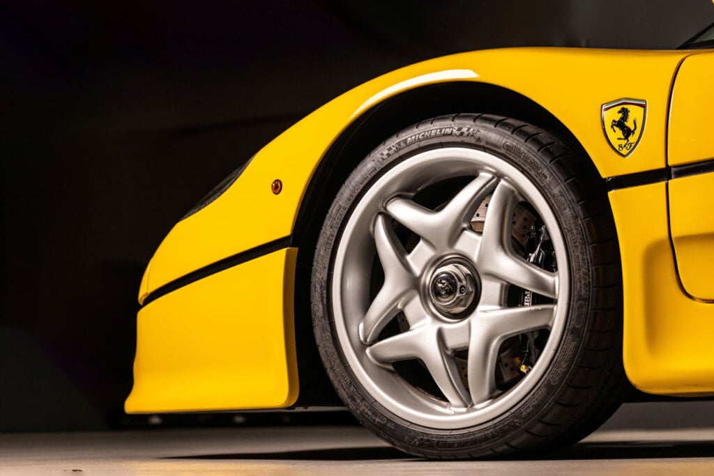 Yellow Ferrari 5 spoke wheel parked inside of a garage. Background is black behind the car