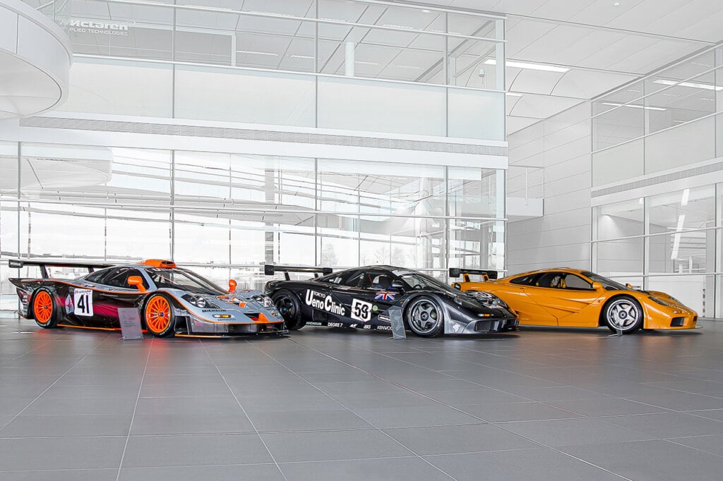 3 McLaren cars next to each other in a white showroom floor, glass windows surround the cars