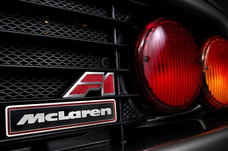 red McLaren F1 Badge on the rear grill of the car next to a red and orange taillight