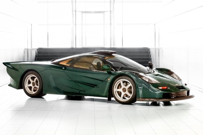 Green McLaren F1 Long Tail GT parked in an all white showroom with gold wheels parked diagonally