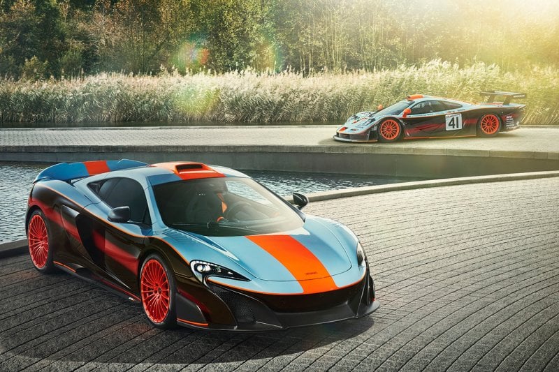 Orange and blue Ueno Clinic McLaren F1 behind a McLaren 675LT with the same livery. Pond and garden next to them