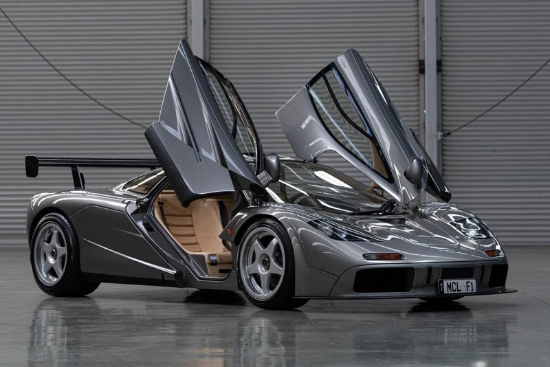 Silver McLaren F1 parked in a warehouse garage with doors open and tan interior