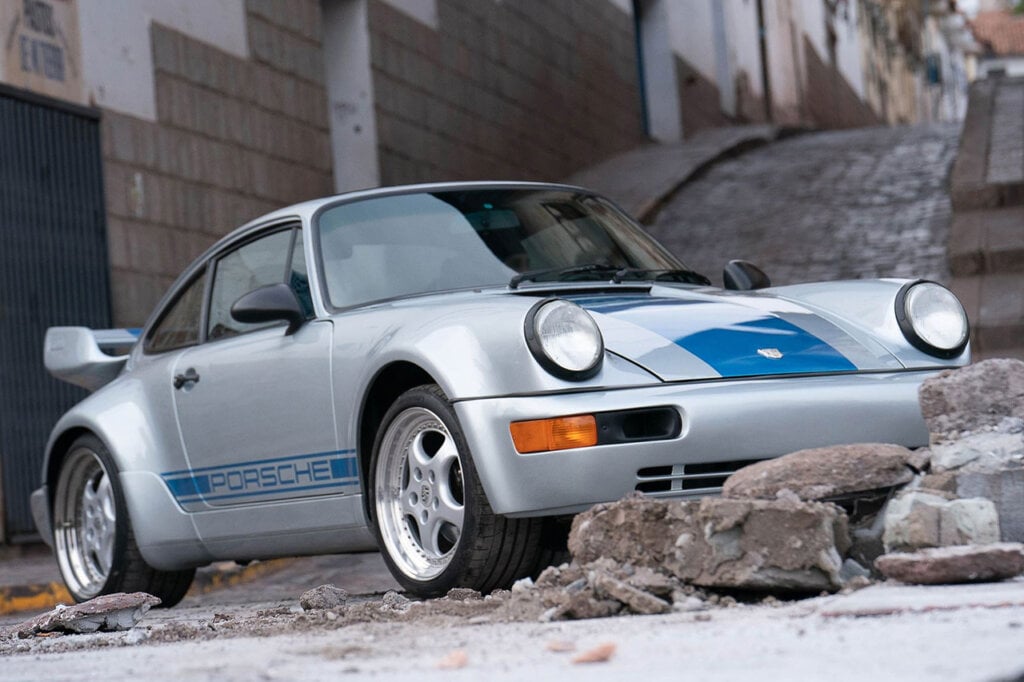 Porsche 911 Carrera RS silver and blue next to big rocks and ruble