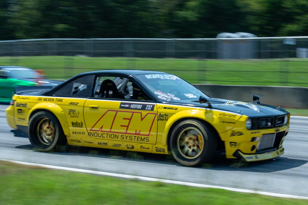 Yellow and Black AEM racing livery on Nissan S14 driving on a racetrack