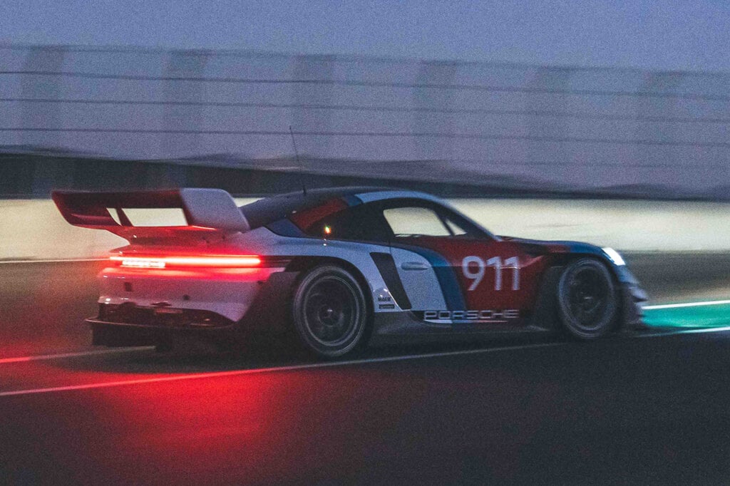 Porsche 911 GT3 R Rennsport driving on a racetrack at night, lights are on 
