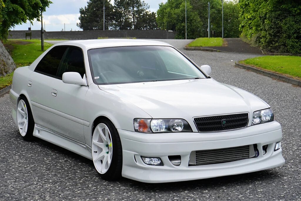 White 6th gen Toyota Chaser parked on a street with grass and trees in background