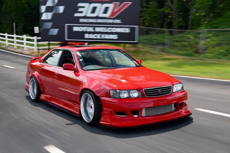 red Toyota Chaser driving past a billboard in the background