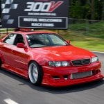 red Toyota Chaser driving past a billboard in the background