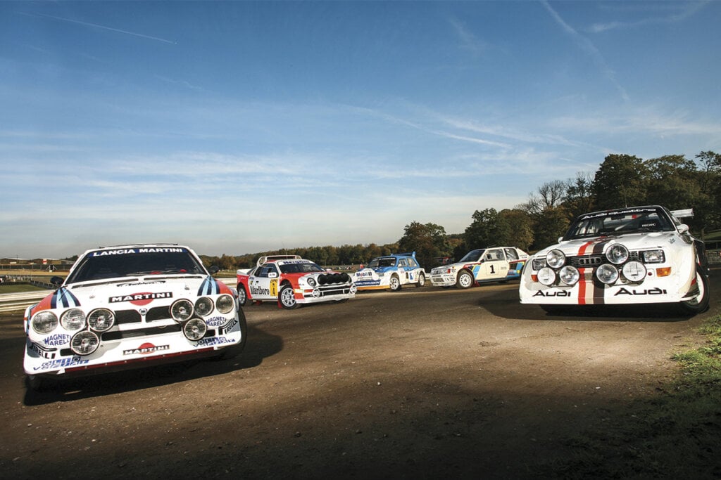 Group B rally race cars parked in a line next to one another with blue sky in background