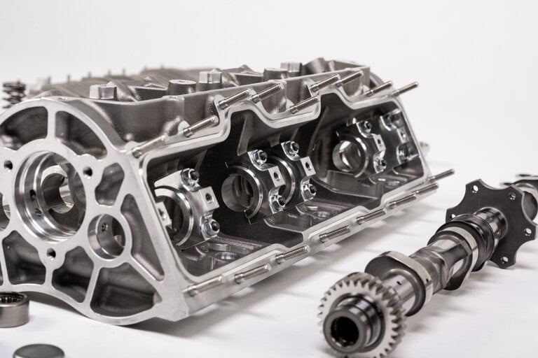 Engine block opened up with camshaft laying flat next to it on white background