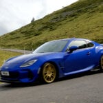 Blue BRZ Touge Edition with gold wheels drifting through a turn with a grassy mountain in the background