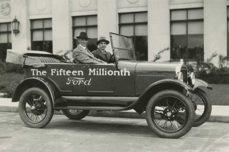 Henry Ford and Edsel Ford sitting in a Ford Model T that says Fifteenth Million Ford on the side of it