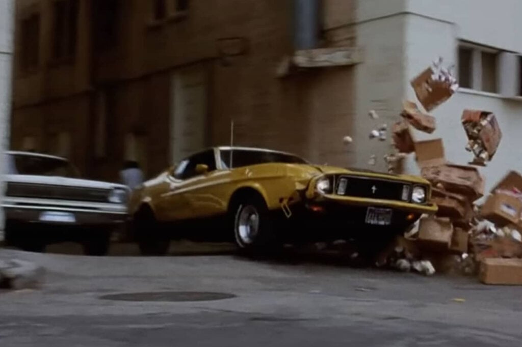 Yellow Ford mustang crashing through boxes and getting chased by another car