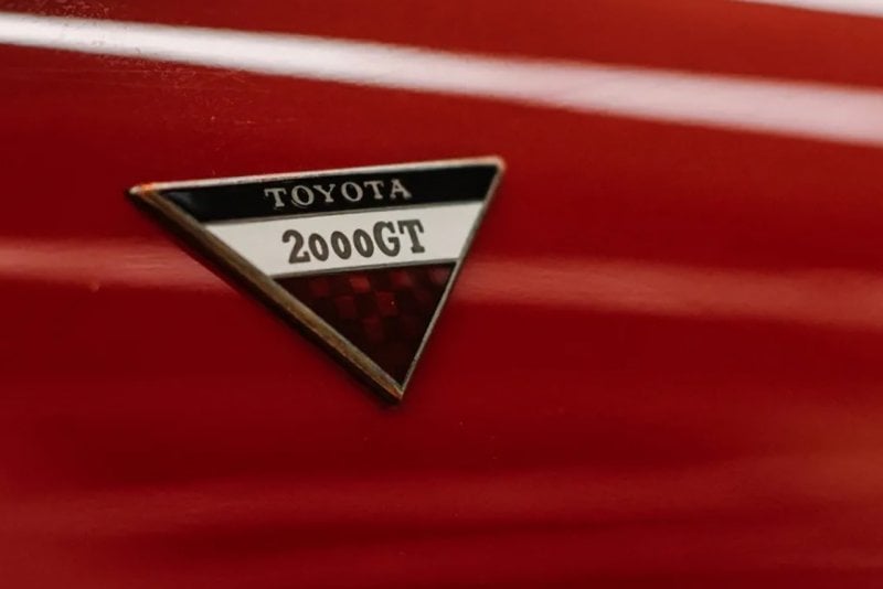 Closeup of an upside down triangle with the words Toyota 2000GT on a red car panel