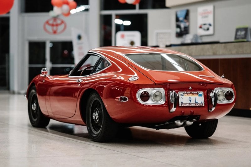 rear shot of a red Toyota 2000GT parked next to a desk in a showroom floor