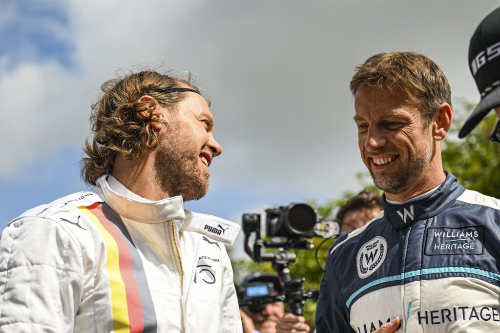 two men talking in racing suits with a camera filming them