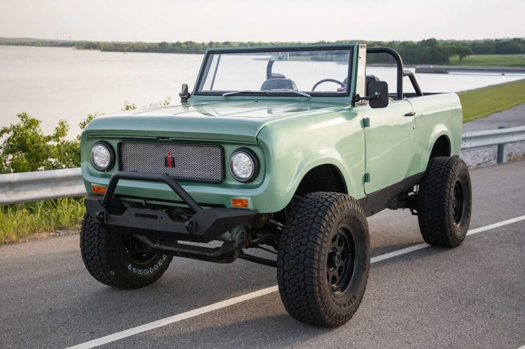 Green lifted Scout 800 parked on the side of the road next to a body of water